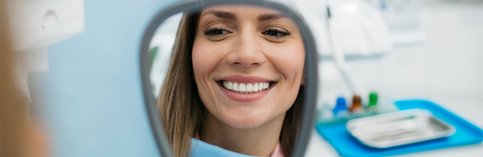 woman-at-dental-office-smiling-in-mirror-1600x522.webp