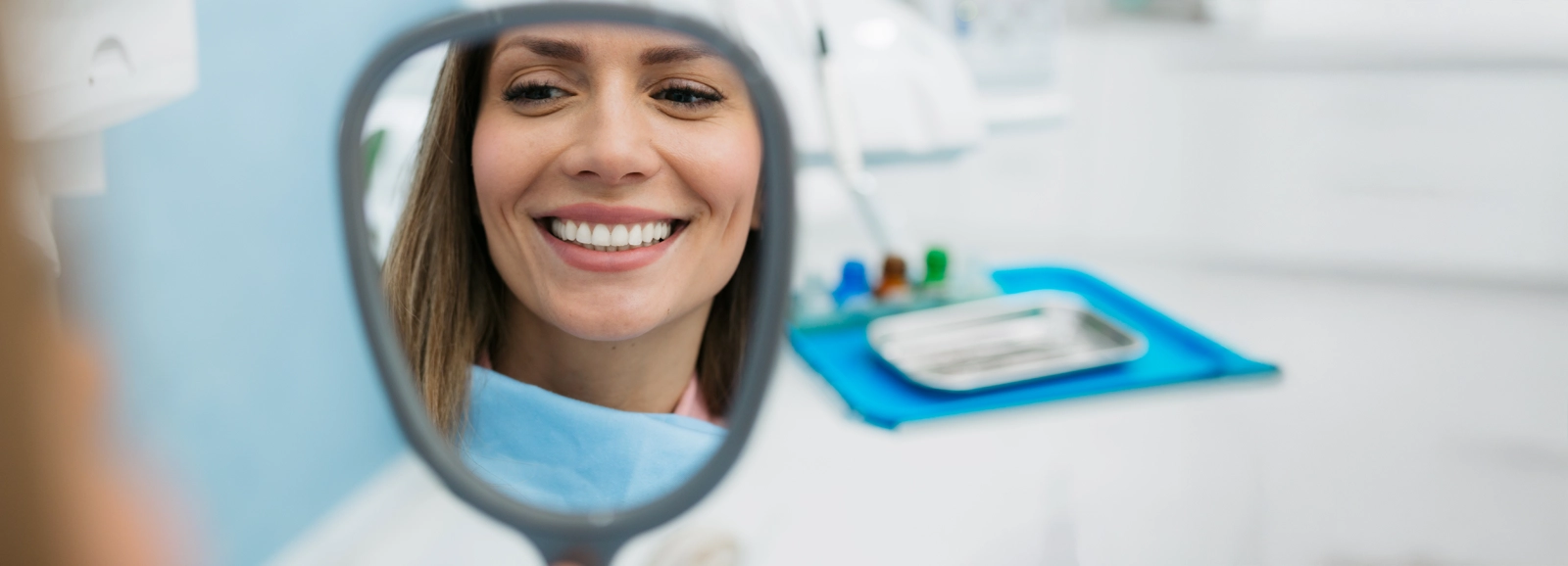 woman-at-dental-office-smiling-in-mirror-1600x578_alt.webp