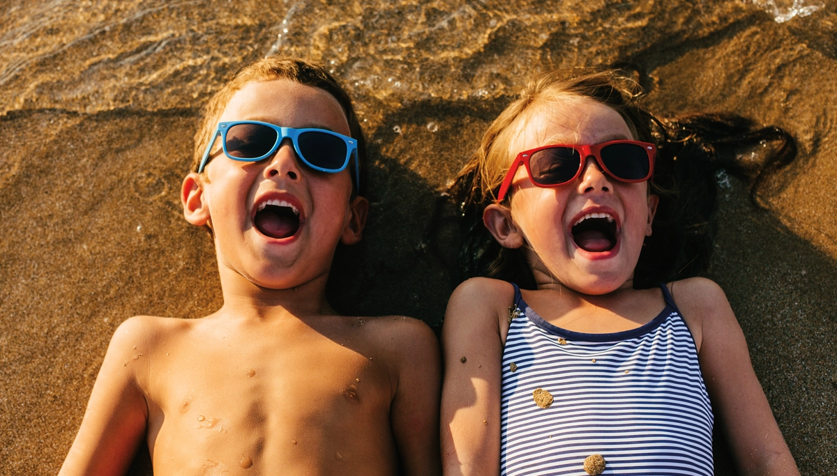 kids-in-sunglasses-laying-in-sand-1200x683.webp