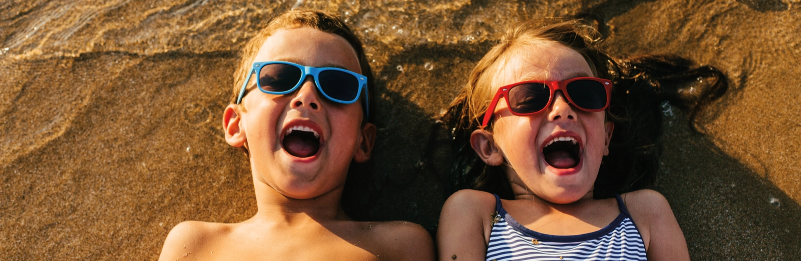 kids-in-sunglasses-laying-in-sand-1600x522.webp