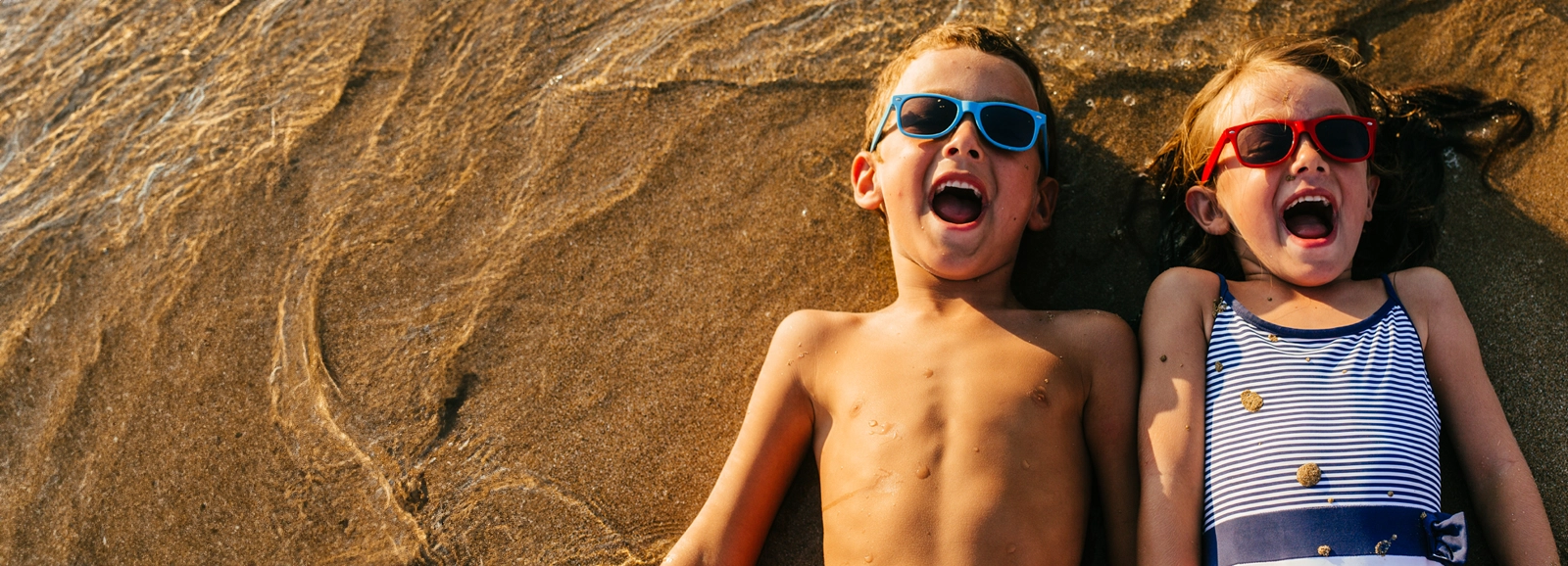 kids-in-sunglasses-laying-in-sand-1600x578-2_rev.webp