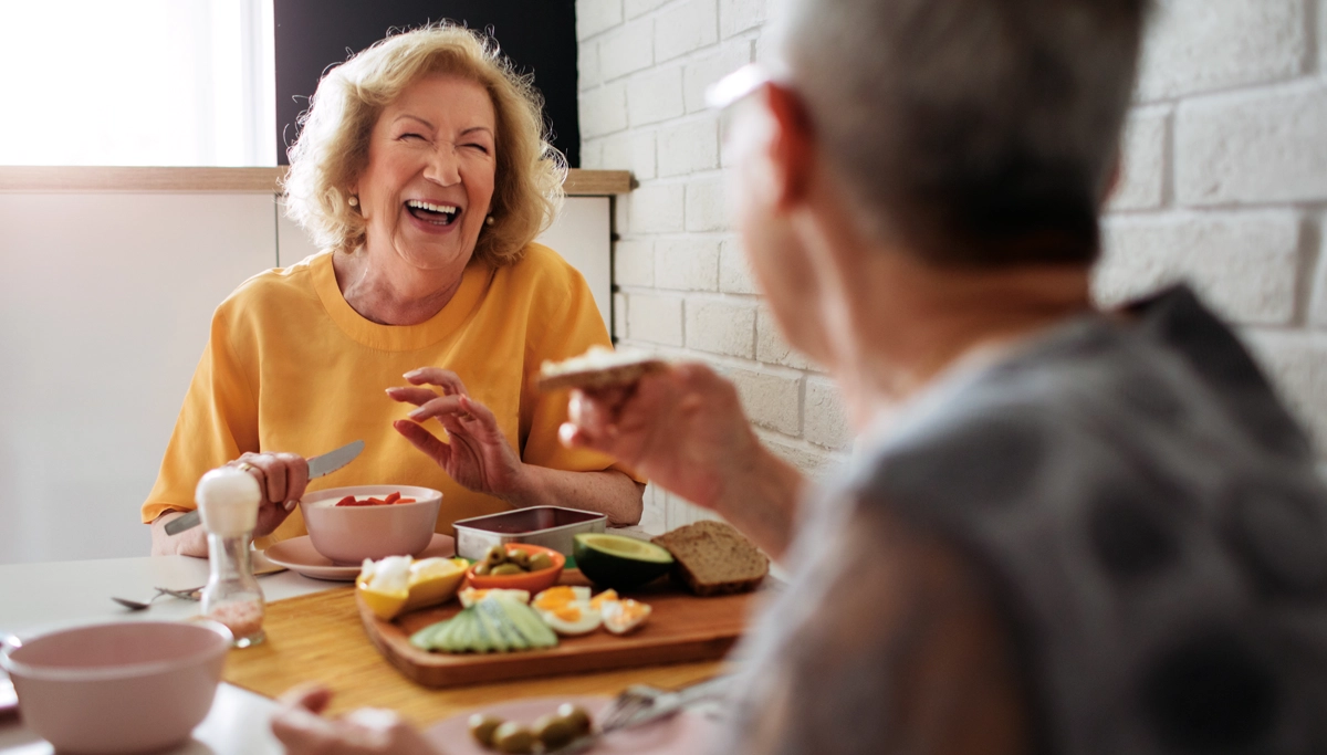 older-couple-laughing-while-eating-breakfast-1200x683.webp