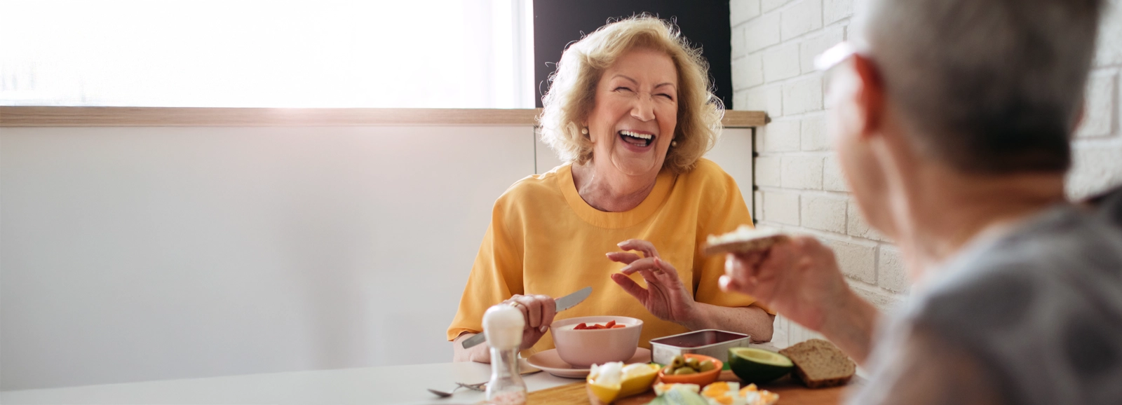 older-couple-laughing-while-eating-breakfast-1600x578-ALT.webp